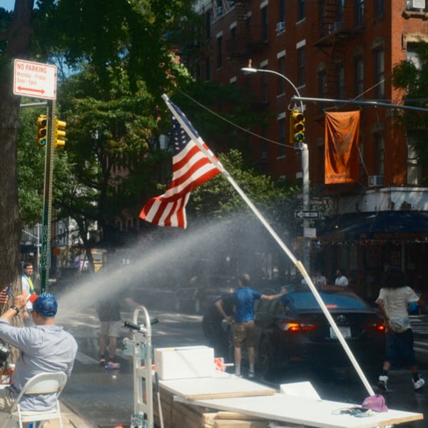A man in a blue hat is standing in front of a fire hydrant that is spraying water.