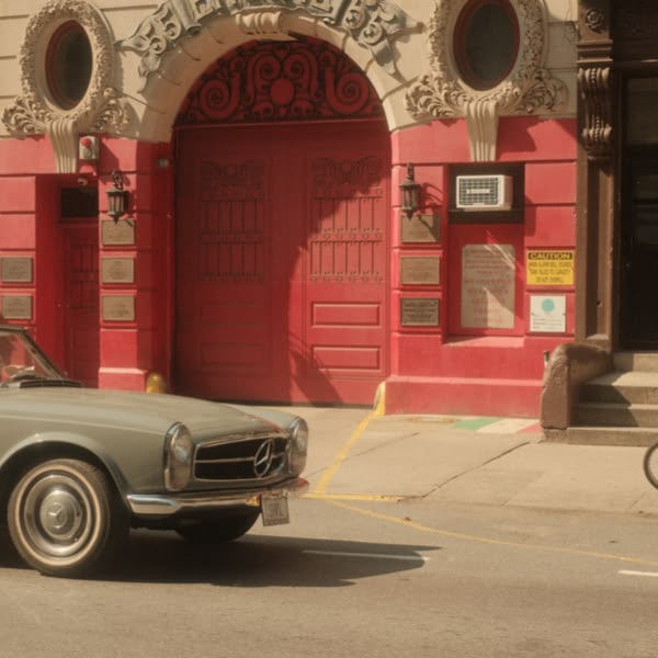 A grey car is parked in front of a red building.