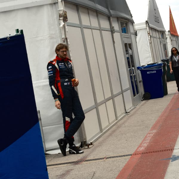 A man in a blue and red racing suit stands in front of a white tent.