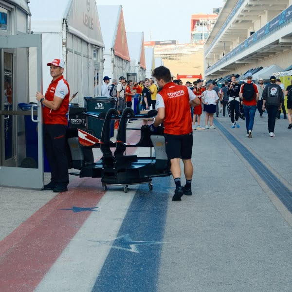 A man in a red shirt is pushing a cart with a car on it.