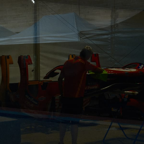 A man in a red shirt is standing next to a red race car.