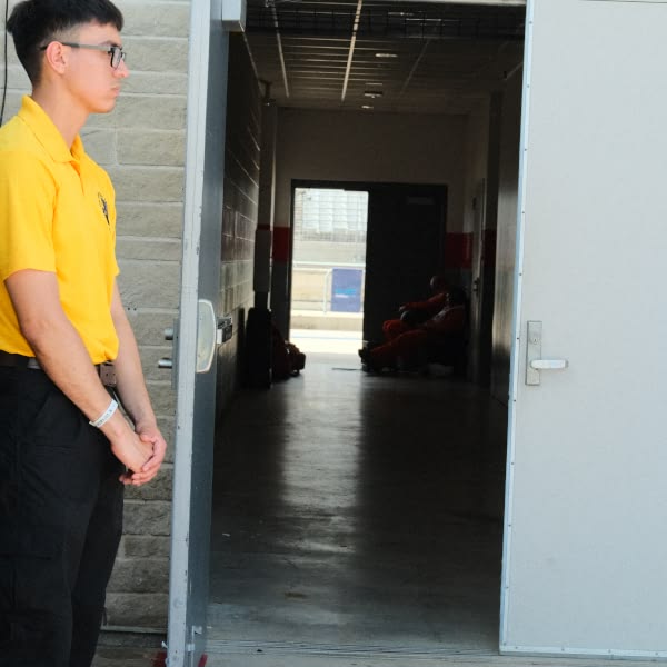 A man wearing a yellow shirt standing in front of a door.