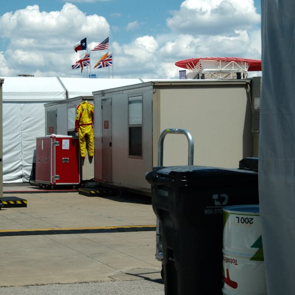 A man in a yellow jumpsuit is standing next to a red suitcase.