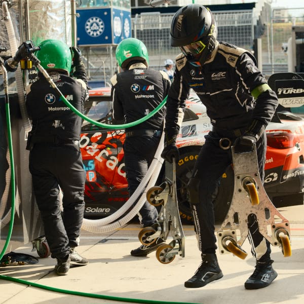 A man wearing a black helmet and black suit is standing next to a car.
