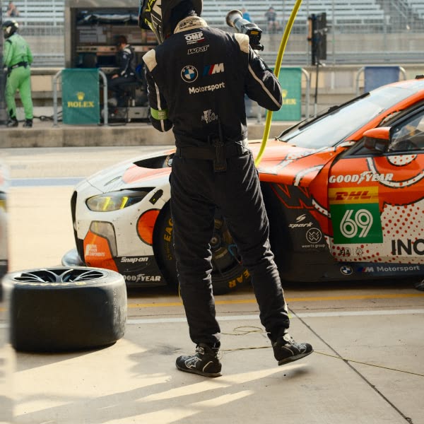A man in a black suit is standing next to a racing car.