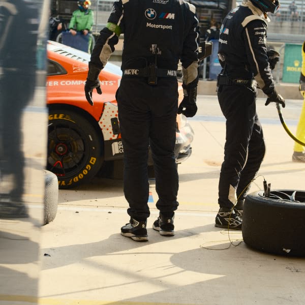 Two men in black suits standing next to a car.