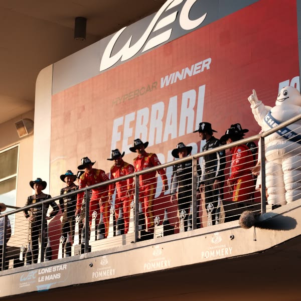 A group of men wearing cowboy hats and red jumpsuits stand on a balcony.