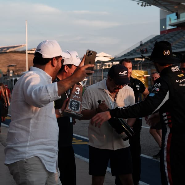 A group of men standing on a track with a man holding a bottle of champagne.