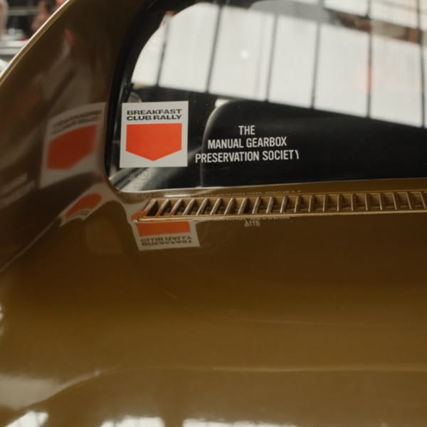 A brown car with a manual preservation society sticker.