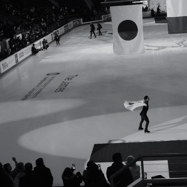A man in a white cape skates on ice.