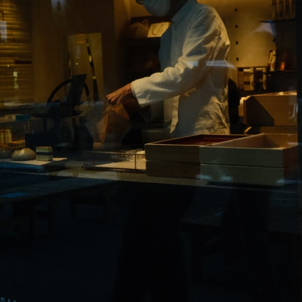 A man wearing a white shirt and mask is holding a brown bag.