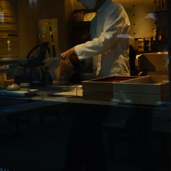 A man wearing a white shirt and mask is holding a brown bag.