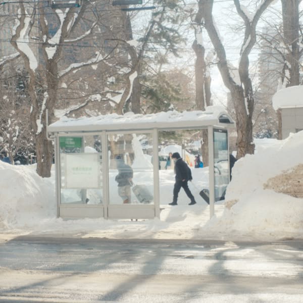 A man walking in front of a bus stop.