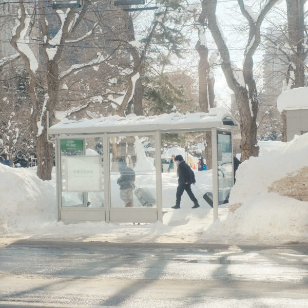 A man walking in front of a bus stop.