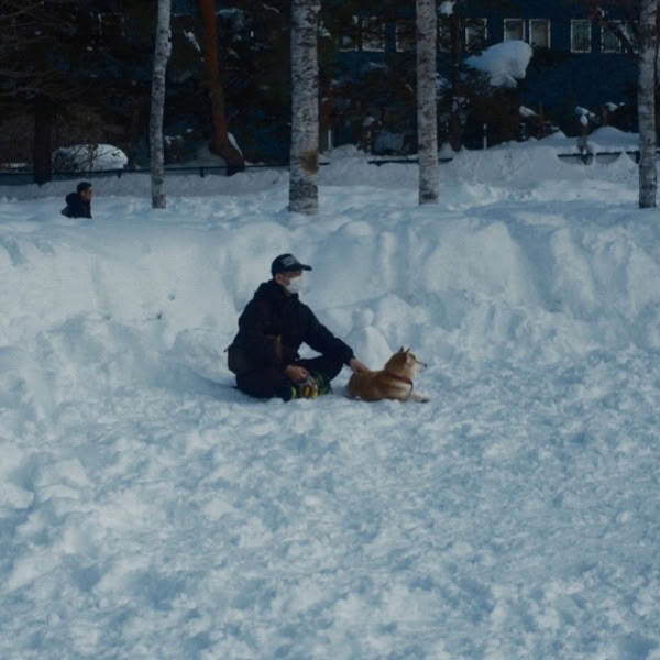 A man sitting in the snow with a dog.