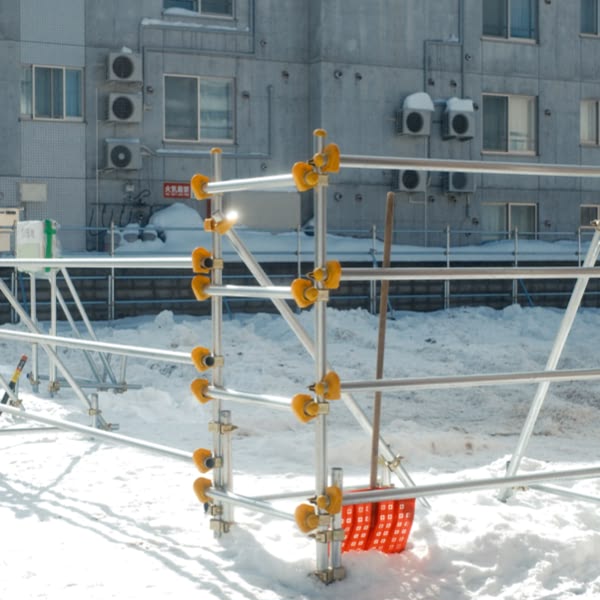 A red and yellow snow shovel is leaning against a metal fence.
