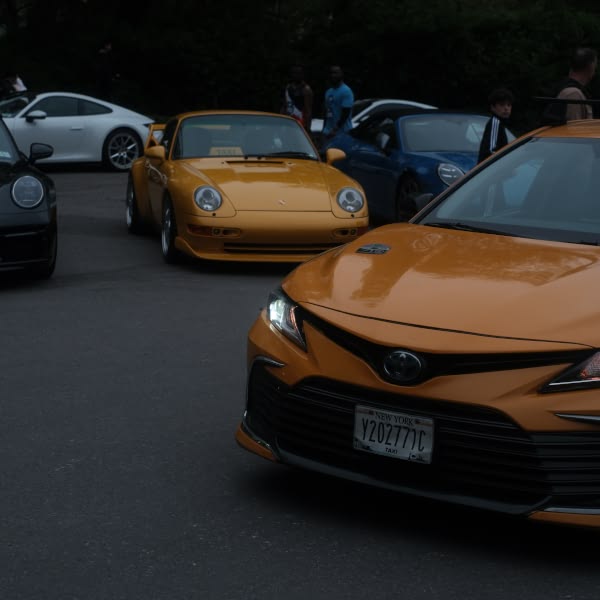 A yellow car is parked in front of a group of other cars.