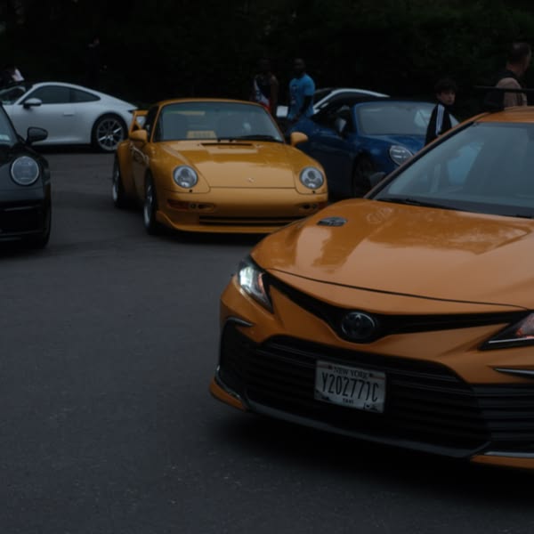 A yellow car is parked in front of a group of other cars.