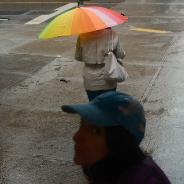 A woman wearing a blue hat and holding a colorful umbrella.