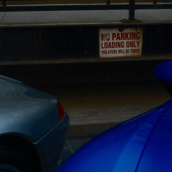 A blue car is parked next to a sign.
