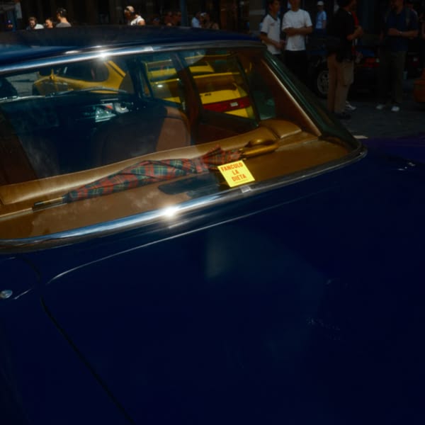 A blue car with a yellow taxi in front of it.