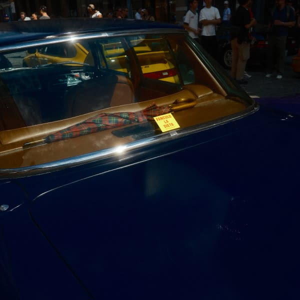 A blue car with a yellow taxi in front of it.